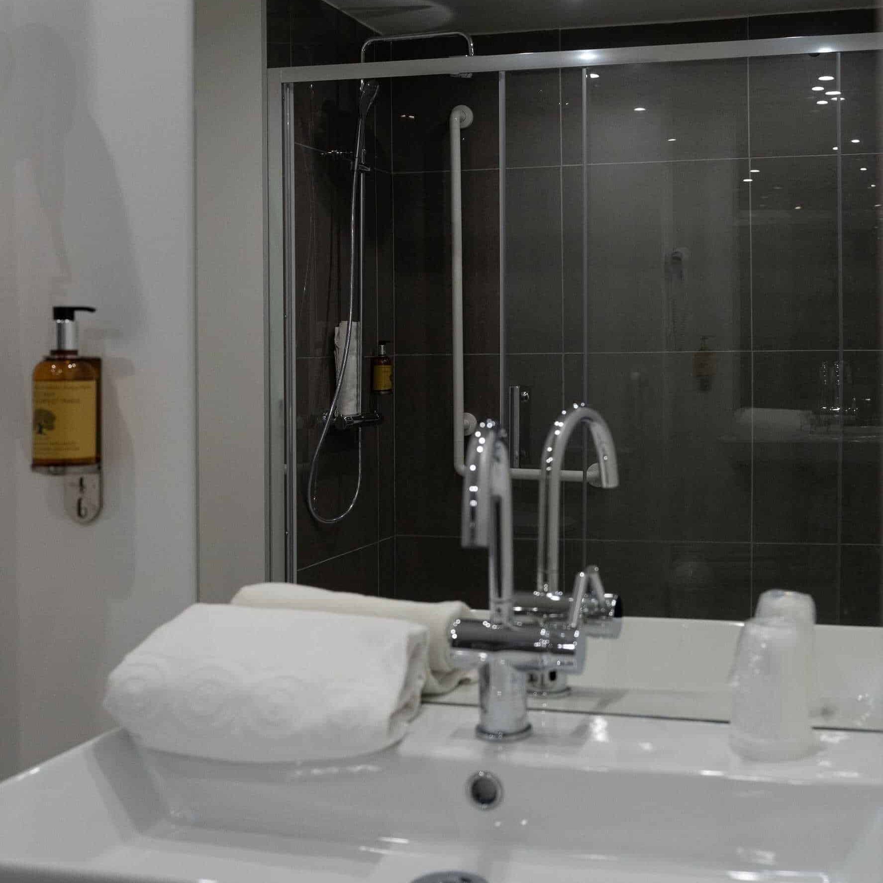 Salle de bain moderne avec douche, lavabo et serviettes à l'Hôtel Libéra à Colombelles.