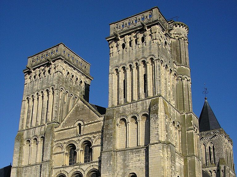 L'abbaye aux Dames, église romane avec deux tours, façade sculptée, située sous un ciel bleu.