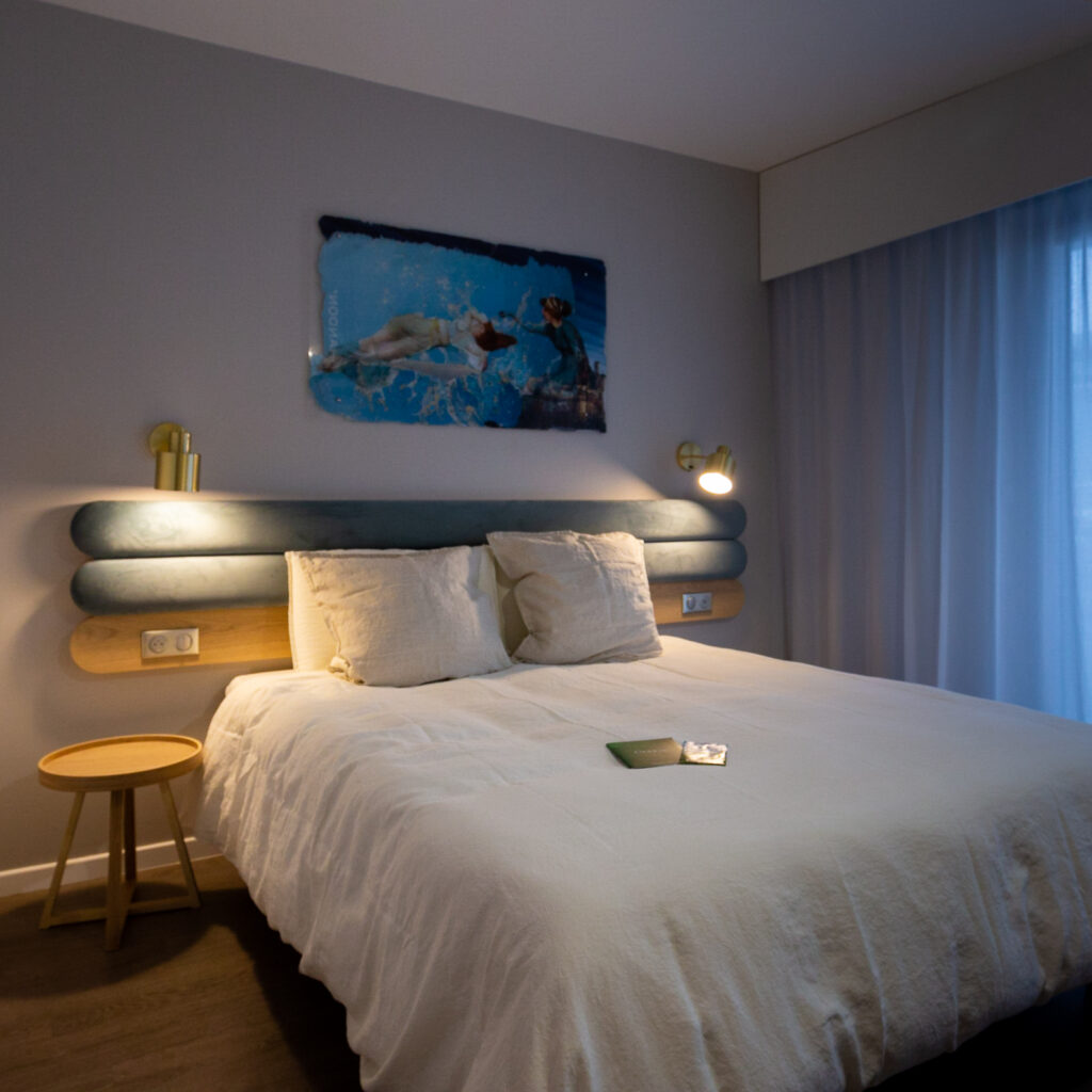 Chambre moderne de l'Hôtel Libéra à Colombelles, avec lit confortable, éclairage contemporain et décoration minimaliste.