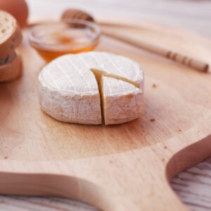 Plateau en bois avec le fromage Livarot, pain, œuf et miel.