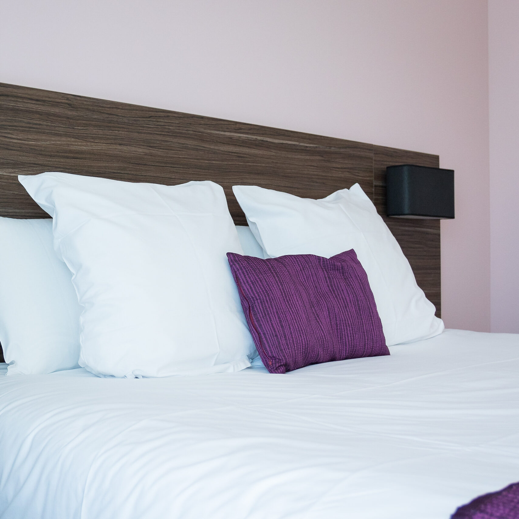 Lit confortable avec oreillers blancs et coussin violet dans une chambre moderne de l'Hôtel Libéra à Colombelles.