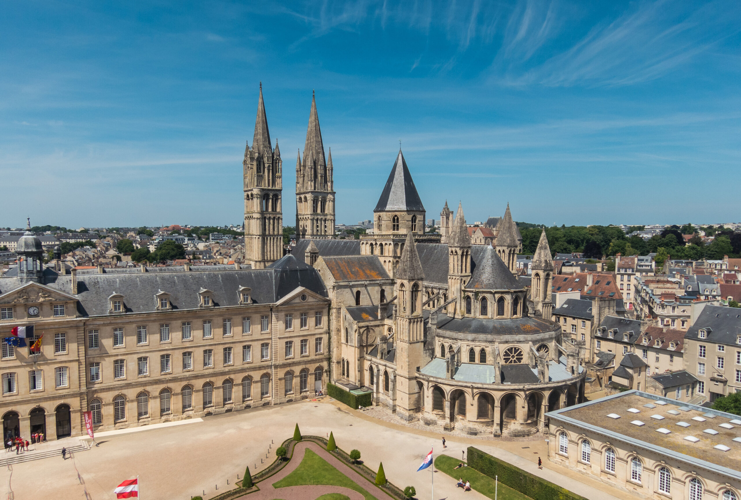 Vue aérienne de l'architecture historique de Caen, avec des tours et des bâtiments anciens sous un ciel ensoleillé.