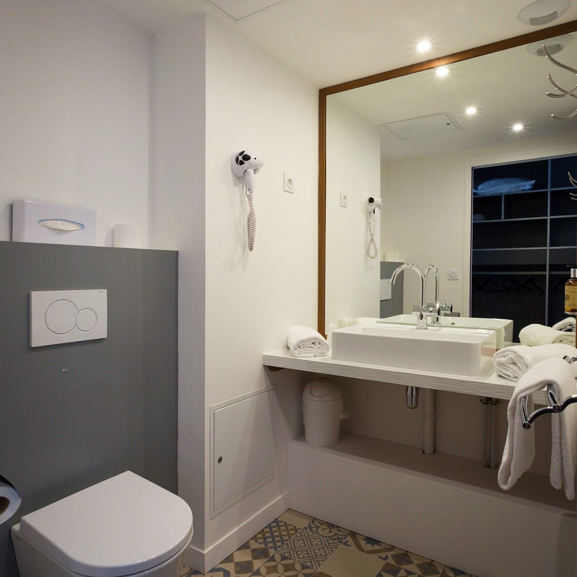 Salle de bain moderne et spacieuse de l'Hôtel Libéra, avec lavabo, toilette et décor au sol élégant.