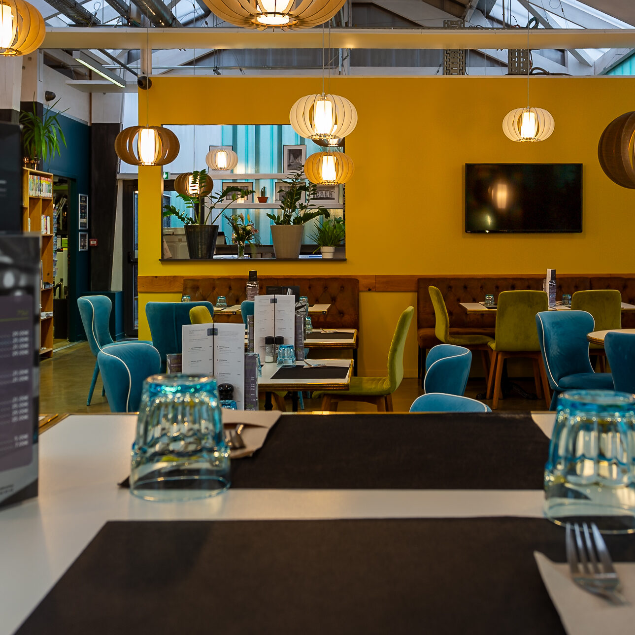 Intérieur moderne et convivial du restaurant de l'Hôtel Libéra, avec des tables, des chaises colorées et une décoration industrielle.