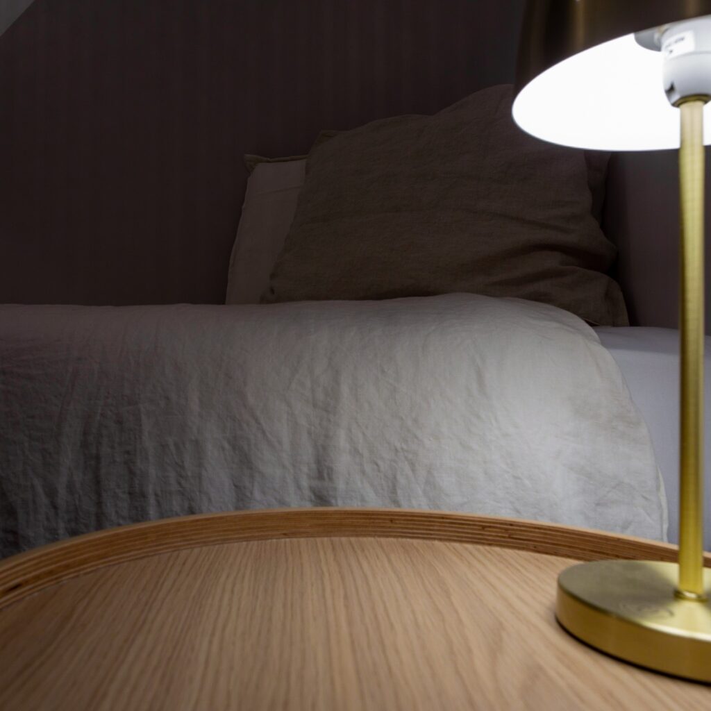 Coin d'une chambre moderne avec un lit, un coussin et une lampe de table sur une table en bois.