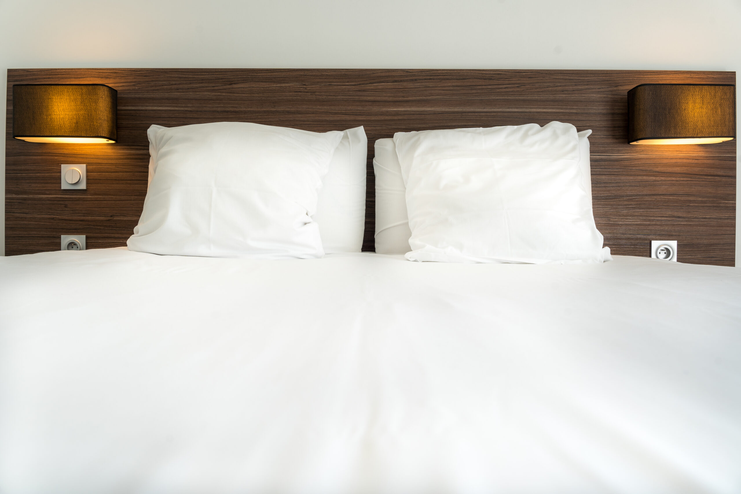 Lit confortable de l'hôtel Libéra avec draps blancs et oreillers, dans une chambre d'hôtel moderne. Appliques lumineuses de chaque côté.